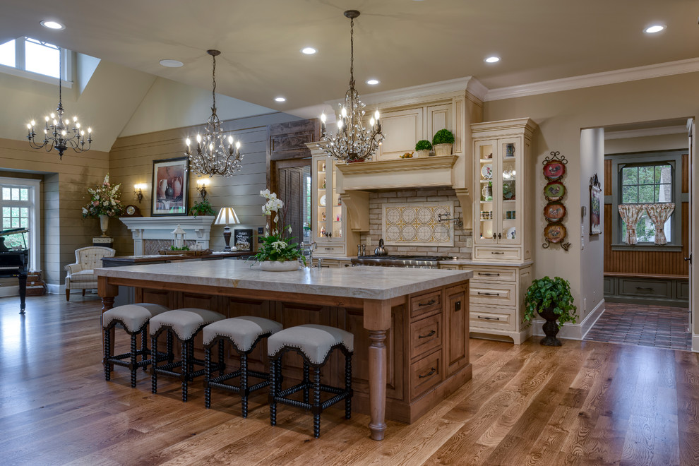 Design ideas for an expansive country l-shaped kitchen pantry in Other with a farmhouse sink, raised-panel cabinets, beige cabinets, granite benchtops, beige splashback, ceramic splashback, panelled appliances, medium hardwood floors, with island, brown floor and beige benchtop.