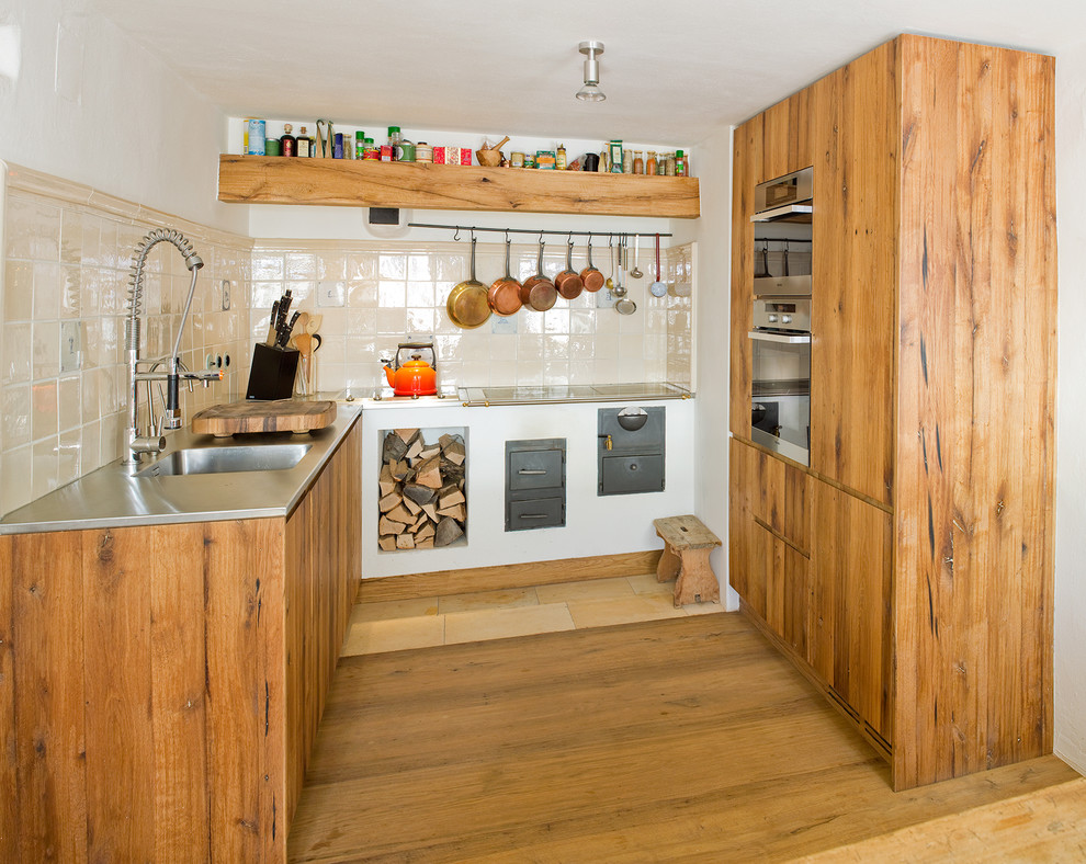 Inspiration for a small country u-shaped kitchen in Other with an integrated sink, stainless steel benchtops, flat-panel cabinets, beige splashback, stainless steel appliances, light wood cabinets and medium hardwood floors.