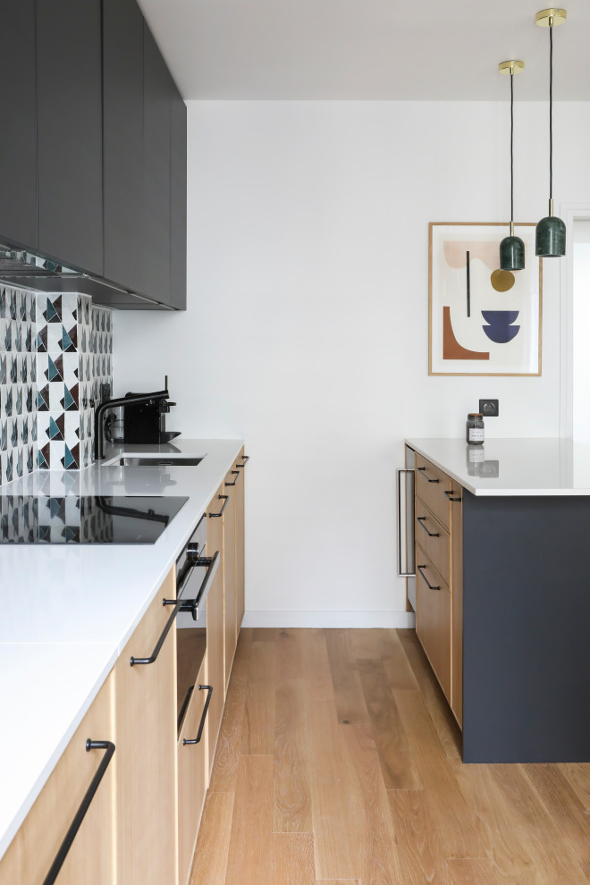 This is an example of a mid-sized contemporary galley kitchen in Paris with an undermount sink, flat-panel cabinets, light wood cabinets, multi-coloured splashback, black appliances, medium hardwood floors, a peninsula, beige floor and white benchtop.