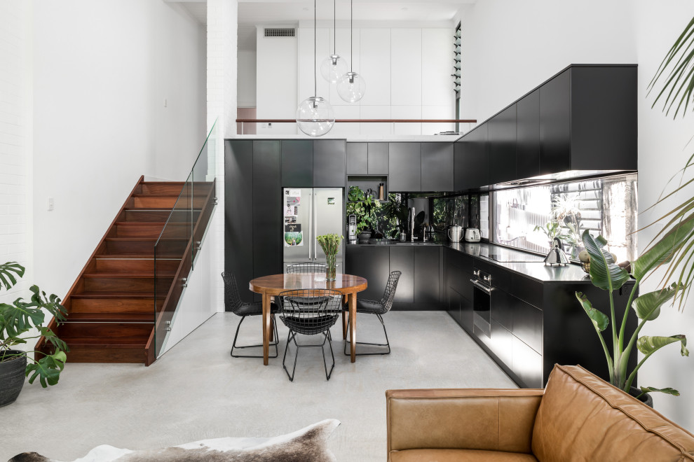 Design ideas for a contemporary l-shaped open plan kitchen in Perth with flat-panel cabinets, black cabinets, stainless steel appliances, concrete floors, no island, grey floor and black benchtop.