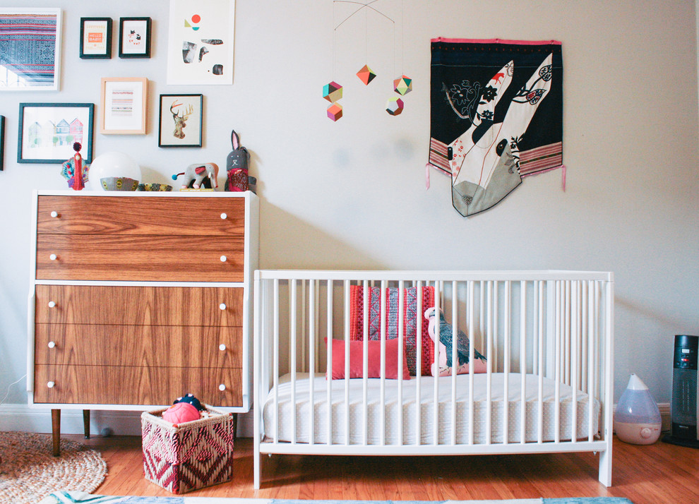 Photo of a small eclectic nursery for girls in San Francisco with white walls and medium hardwood floors.