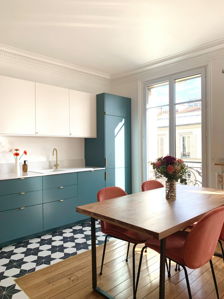 This is an example of a large modern l-shaped open plan kitchen in Paris with a single-bowl sink, beaded inset cabinets, blue cabinets, quartz benchtops, white splashback, engineered quartz splashback, black appliances, cement tiles, no island, black floor and white benchtop.