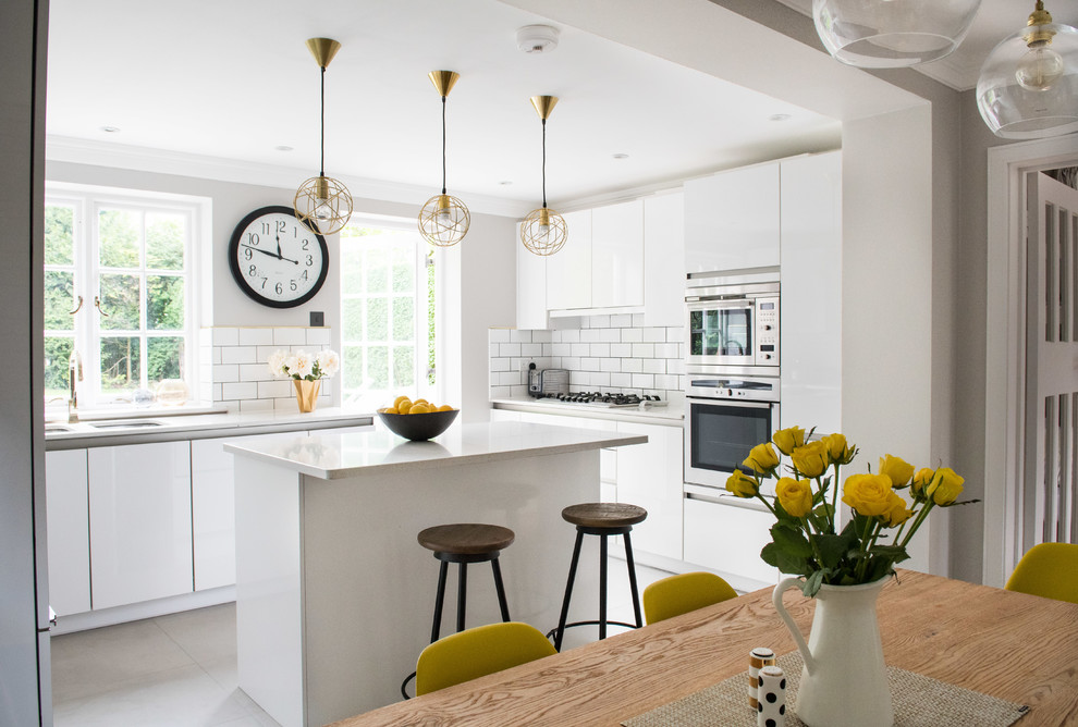 Inspiration for a mid-sized contemporary u-shaped eat-in kitchen in London with a double-bowl sink, flat-panel cabinets, white cabinets, white splashback, subway tile splashback, stainless steel appliances, with island, grey floor and white benchtop.