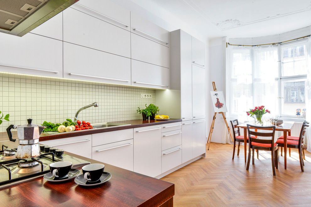 Photo of a large traditional l-shaped separate kitchen in Other with flat-panel cabinets, white cabinets, laminate benchtops, white splashback, ceramic splashback, stainless steel appliances and light hardwood floors.