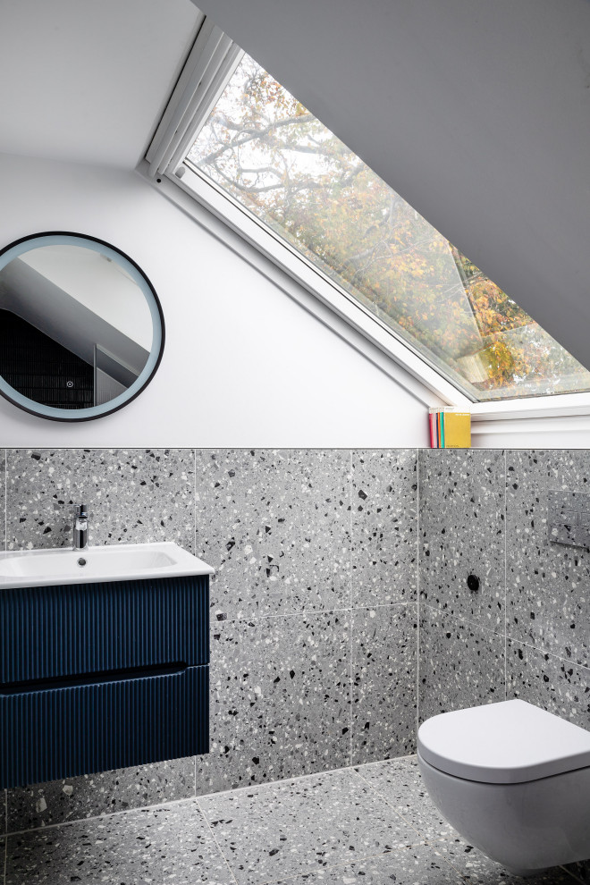 Modernes Badezimmer mit flächenbündigen Schrankfronten, blauen Schränken, grauen Fliesen, weißer Wandfarbe, grauem Boden, Einzelwaschbecken, schwebendem Waschtisch und gewölbter Decke in Hertfordshire