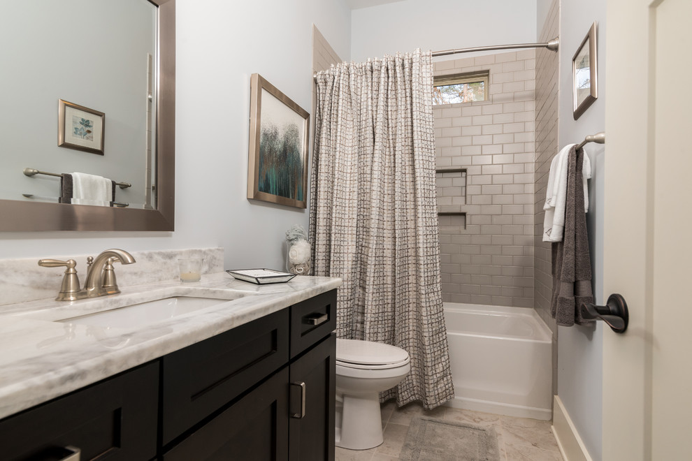 Design ideas for a mid-sized traditional 3/4 bathroom in Charlotte with shaker cabinets, black cabinets, an alcove tub, a shower/bathtub combo, a two-piece toilet, gray tile, subway tile, white walls, travertine floors, an undermount sink, quartzite benchtops, beige floor and a shower curtain.