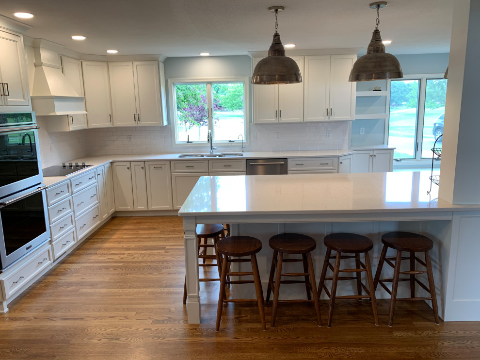 Open concept kitchen - large transitional u-shaped medium tone wood floor and brown floor open concept kitchen idea with an undermount sink, recessed-panel cabinets, white cabinets, quartz countertops, white backsplash, stainless steel appliances, an island and white countertops