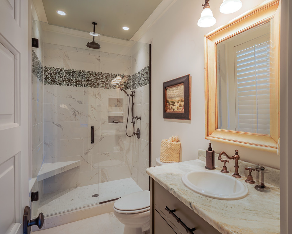 Photo of a mid-sized traditional 3/4 bathroom in Charleston with a one-piece toilet, pebble tile, medium wood cabinets, an alcove shower, blue tile, brown tile, white walls, flat-panel cabinets, marble floors, a drop-in sink, marble benchtops and white floor.
