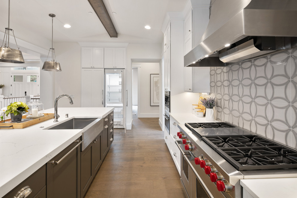 Large arts and crafts single-wall eat-in kitchen in Seattle with a farmhouse sink, shaker cabinets, white cabinets, quartzite benchtops, grey splashback, porcelain splashback, stainless steel appliances, medium hardwood floors, with island, brown floor, white benchtop and exposed beam.