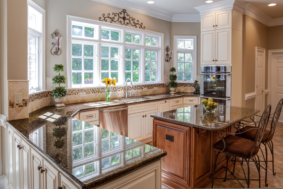 Photo of a large traditional u-shaped eat-in kitchen in Charlotte with a single-bowl sink, raised-panel cabinets, white cabinets, granite benchtops, beige splashback, stone tile splashback, stainless steel appliances, porcelain floors and with island.