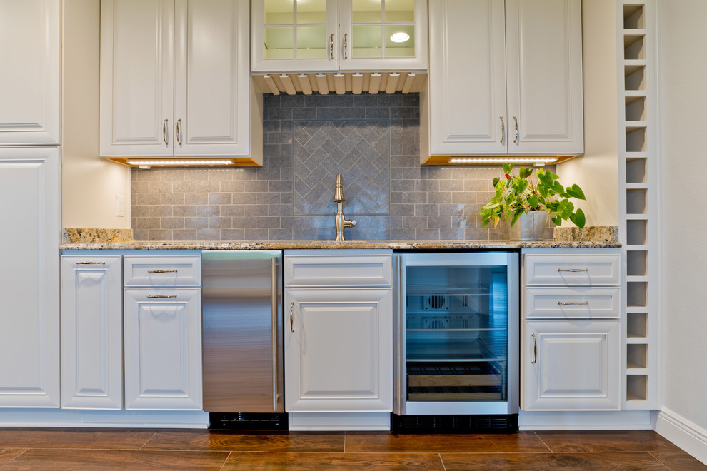 Eat-in kitchen - large transitional galley porcelain tile eat-in kitchen idea in Miami with an undermount sink, raised-panel cabinets, white cabinets, granite countertops, gray backsplash, porcelain backsplash, stainless steel appliances and an island