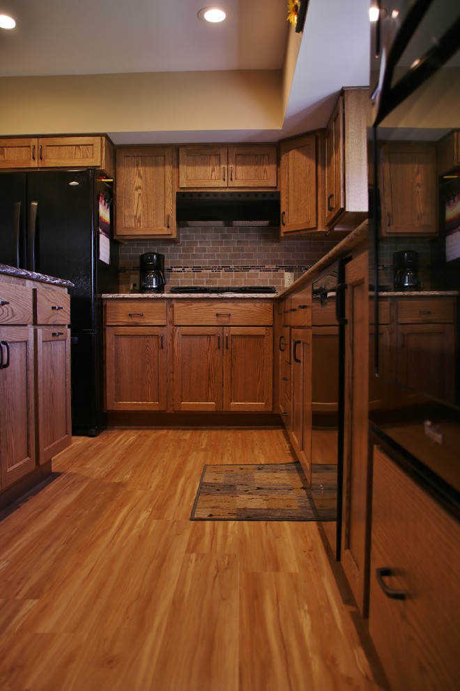 Mid-sized l-shaped eat-in kitchen photo with flat-panel cabinets, medium tone wood cabinets, quartz countertops, beige backsplash, black appliances and an island