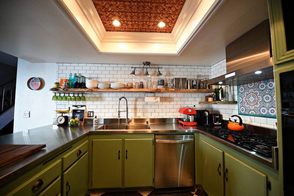 This is an example of a mid-sized eclectic u-shaped eat-in kitchen in Las Vegas with an integrated sink, flat-panel cabinets, green cabinets, stainless steel benchtops, white splashback, ceramic splashback, stainless steel appliances, porcelain floors and no island.