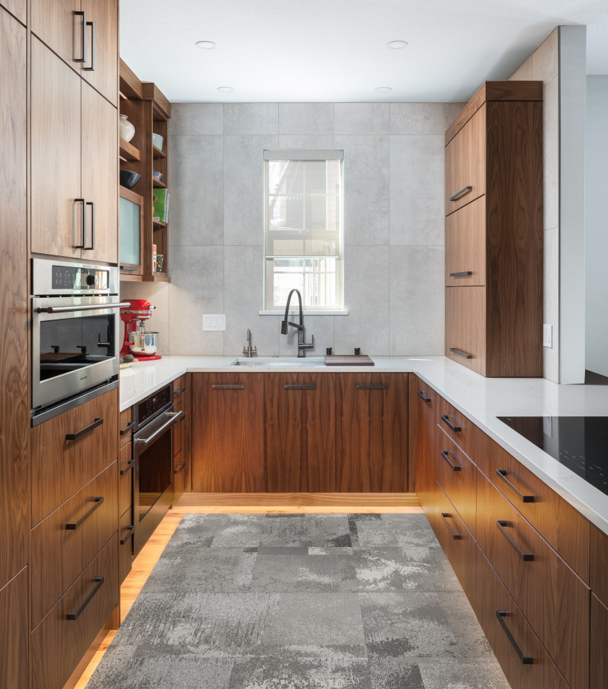 This is an example of a mid-sized contemporary u-shaped open plan kitchen in Other with an undermount sink, flat-panel cabinets, medium wood cabinets, quartz benchtops, grey splashback, ceramic splashback, stainless steel appliances, medium hardwood floors, a peninsula and white benchtop.