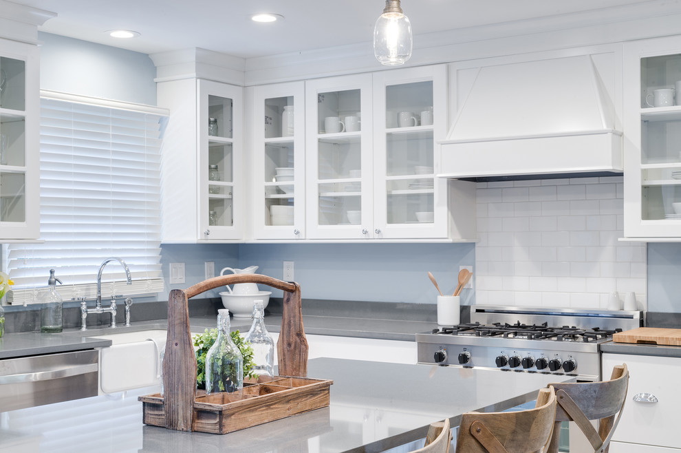 Mid-sized traditional l-shaped eat-in kitchen in Chicago with a farmhouse sink, glass-front cabinets, white cabinets, quartzite benchtops, white splashback, subway tile splashback, stainless steel appliances, light hardwood floors, with island and beige floor.