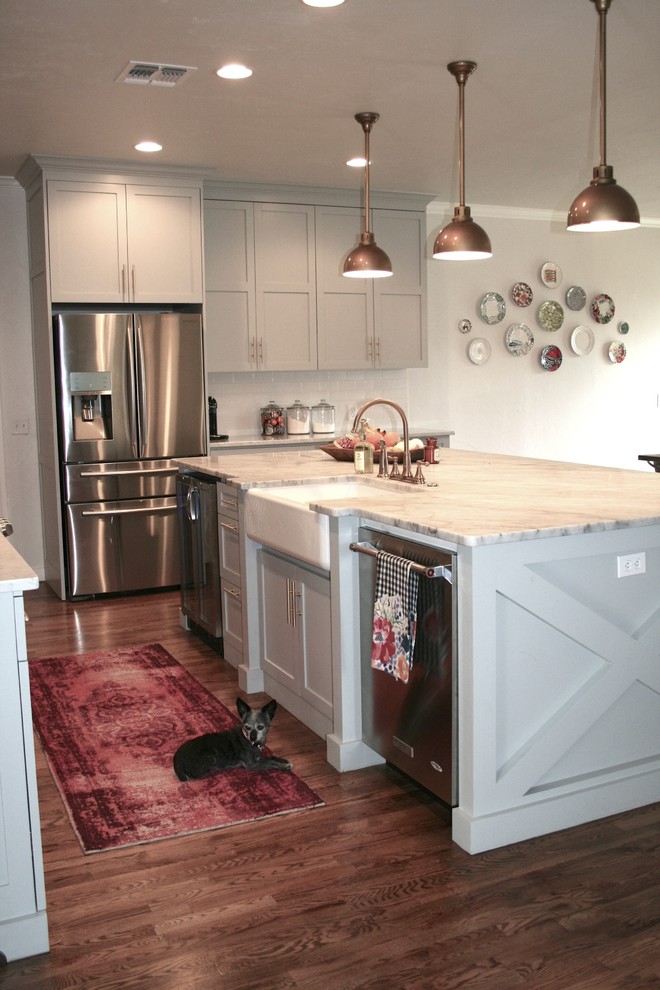 Design ideas for a mid-sized country l-shaped eat-in kitchen in Oklahoma City with a farmhouse sink, flat-panel cabinets, grey cabinets, marble benchtops, white splashback, subway tile splashback, stainless steel appliances, light hardwood floors, with island and brown floor.