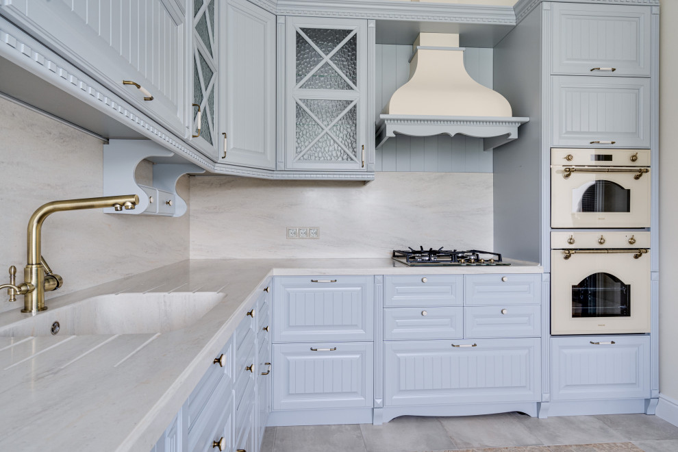 Photo of a mid-sized country l-shaped eat-in kitchen in Moscow with an integrated sink, raised-panel cabinets, grey cabinets, solid surface benchtops, beige splashback, marble splashback, porcelain floors, beige floor and beige benchtop.
