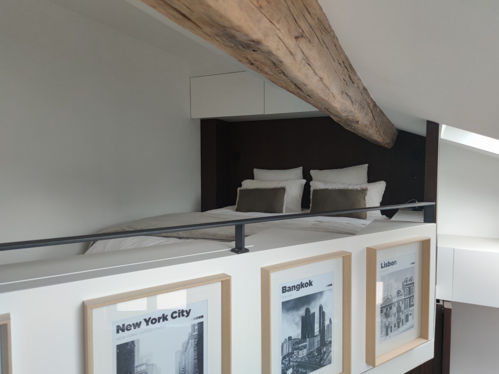 Example of a small minimalist loft-style light wood floor, beige floor, exposed beam and shiplap wall bedroom design in Paris with white walls, a standard fireplace and a stone fireplace