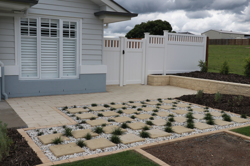 Foto di un grande giardino formale esposto in pieno sole davanti casa in estate con un muro di contenimento, pavimentazioni in cemento e recinzione in PVC