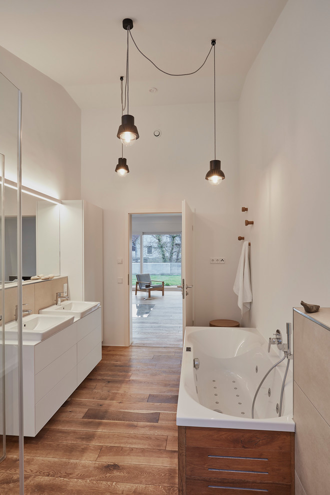 Mid-sized contemporary bathroom in Stuttgart with flat-panel cabinets, white cabinets, a freestanding tub, a curbless shower, white walls, medium hardwood floors, solid surface benchtops, porcelain tile, a vessel sink and brown floor.