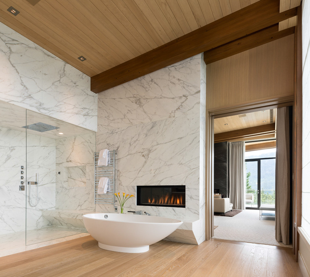 Expansive contemporary master bathroom in Vancouver with flat-panel cabinets, light wood cabinets, a freestanding tub, a double shower, a one-piece toilet, stone slab, white walls, light hardwood floors, a wall-mount sink, marble benchtops and white tile.