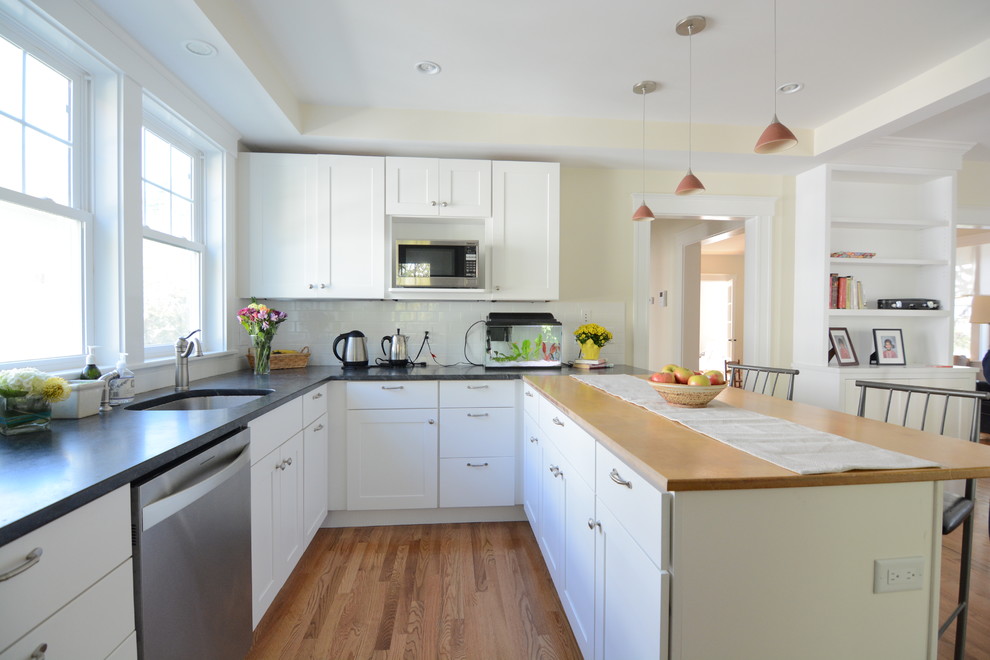 Inspiration for a large transitional l-shaped medium tone wood floor and brown floor kitchen pantry remodel in Boston with a drop-in sink, flat-panel cabinets, white cabinets, solid surface countertops, white backsplash, subway tile backsplash, stainless steel appliances and an island
