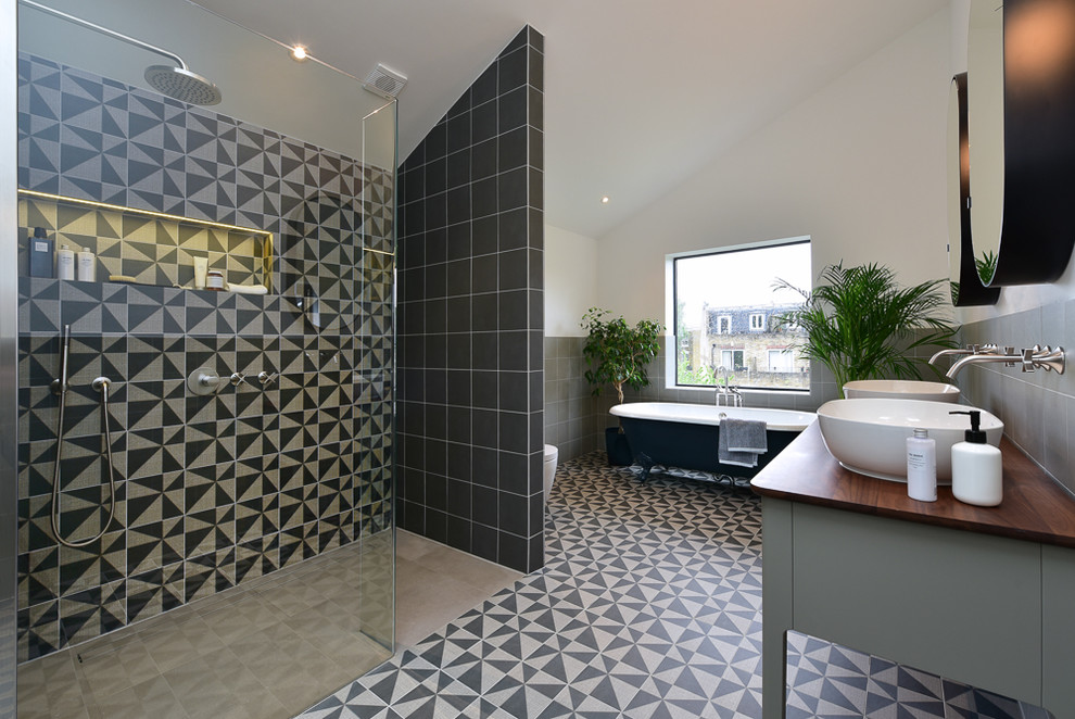 Photo of a large modern bathroom in London with grey cabinets, a claw-foot tub, beige tile, black tile, cement tile, white walls, cement tiles, a vessel sink, wood benchtops, multi-coloured floor and brown benchtops.