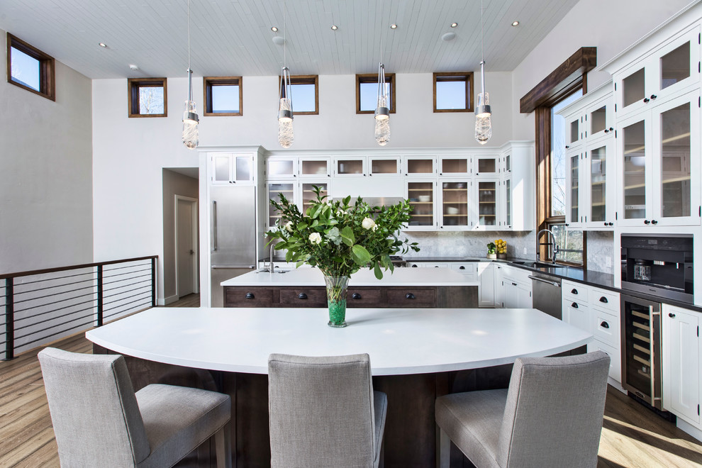 Mid-sized transitional l-shaped light wood floor and beige floor eat-in kitchen photo in Denver with an undermount sink, glass-front cabinets, white cabinets, stainless steel appliances, an island, laminate countertops, gray backsplash and marble backsplash