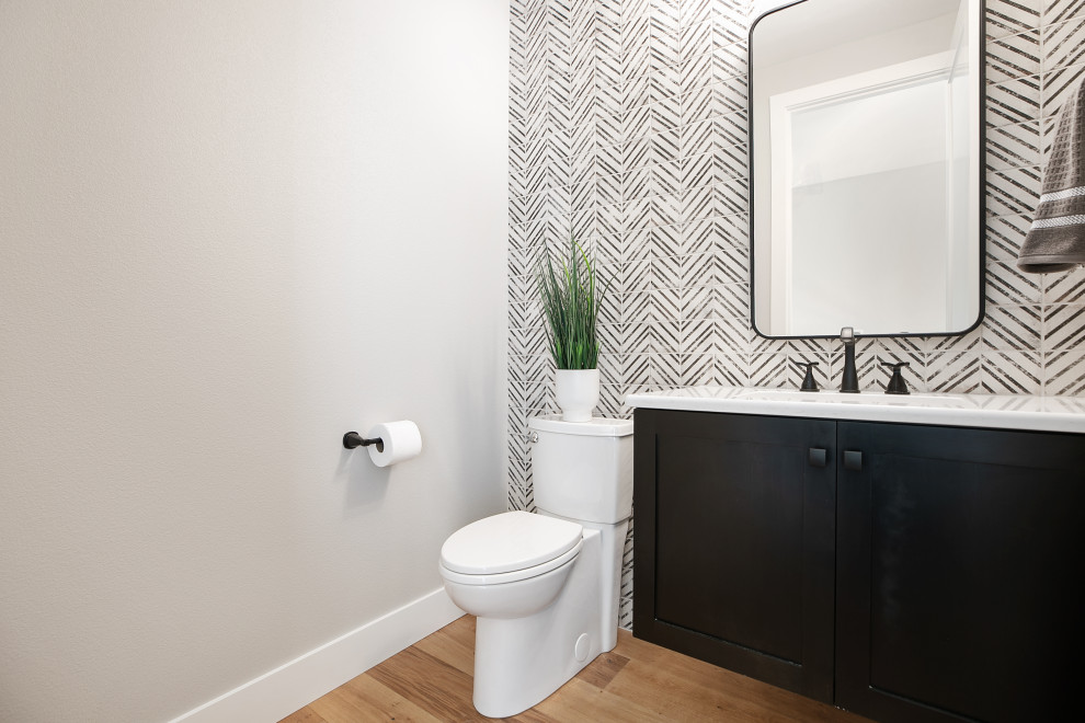 This is an example of a small modern 3/4 bathroom in Portland with shaker cabinets, black cabinets, a one-piece toilet, black and white tile, porcelain tile, white walls, medium hardwood floors, a drop-in sink, engineered quartz benchtops, brown floor, white benchtops, an enclosed toilet, a single vanity and a floating vanity.