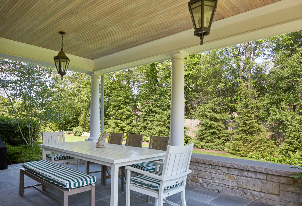 This is an example of a medium sized classic side veranda in Chicago with with columns, natural stone paving and a roof extension.