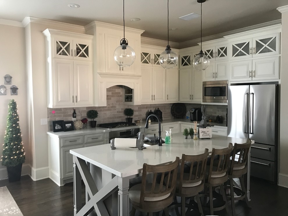 This is an example of a mid-sized country l-shaped open plan kitchen in Austin with raised-panel cabinets, white cabinets, with island, terrazzo benchtops, grey splashback, stone tile splashback, stainless steel appliances, a double-bowl sink, dark hardwood floors and brown floor.