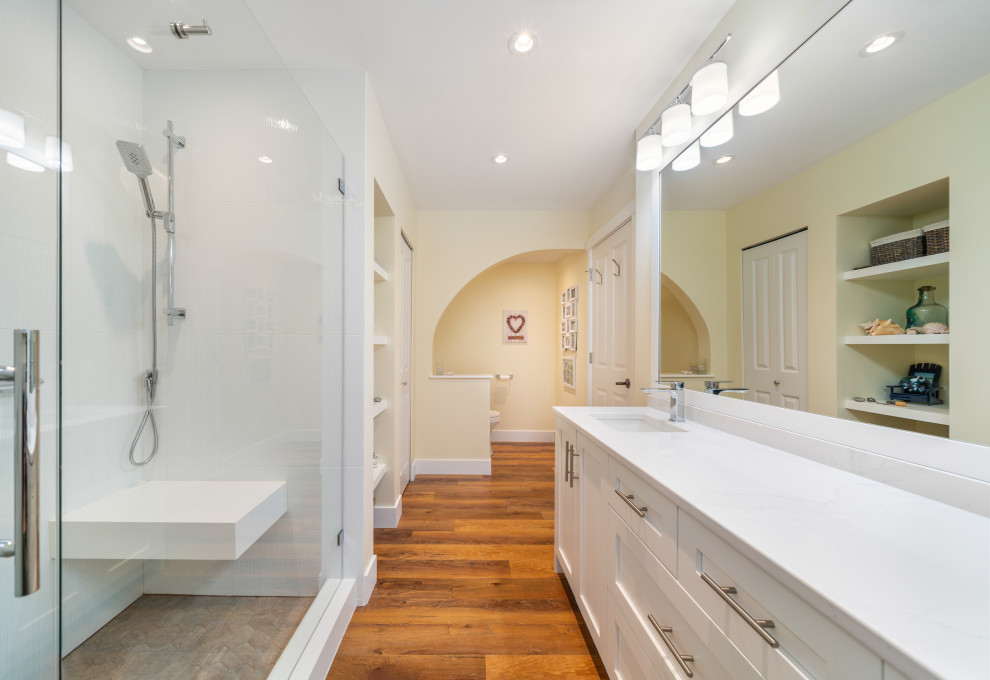 Foto på ett mellanstort maritimt vit en-suite badrum, med skåp i shakerstil, vita skåp, vit kakel, vita väggar, mellanmörkt trägolv, ett undermonterad handfat, bänkskiva i kvarts, brunt golv och dusch med gångjärnsdörr
