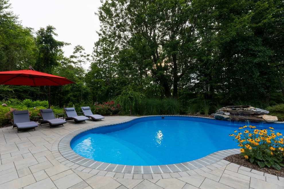 Design ideas for a mid-sized traditional backyard custom-shaped pool in New York with a water feature and concrete pavers.