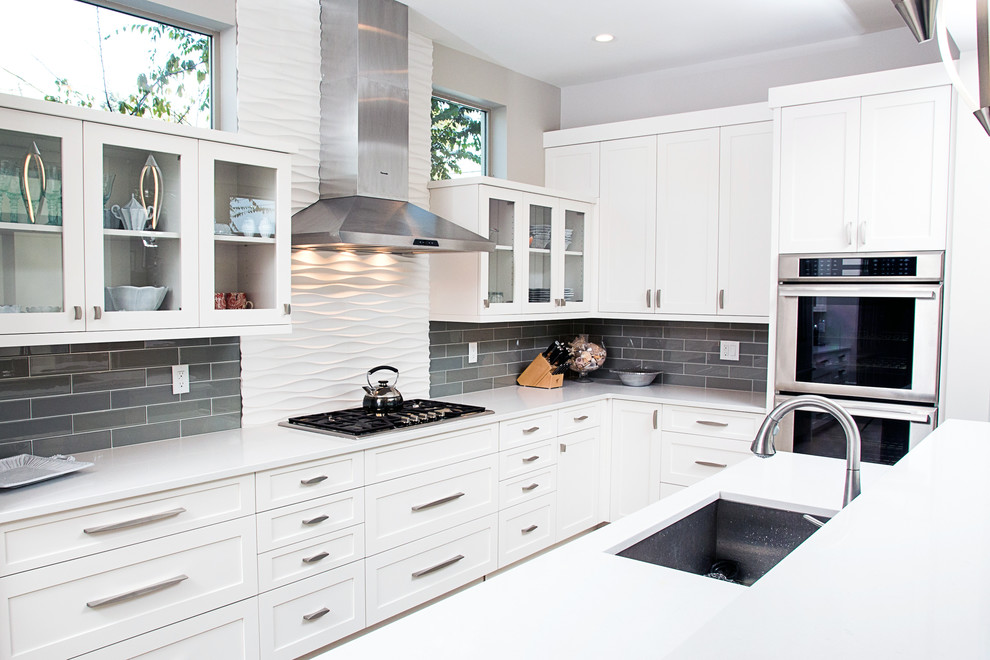 Mid-sized contemporary l-shaped open plan kitchen in Denver with white cabinets, quartz benchtops, grey splashback, glass tile splashback, stainless steel appliances, an undermount sink, with island and shaker cabinets.