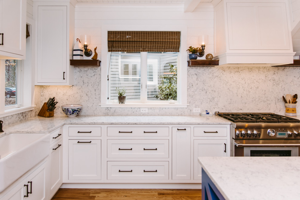 Large beach style u-shaped eat-in kitchen in Baltimore with a farmhouse sink, beaded inset cabinets, white cabinets, quartz benchtops, white splashback, engineered quartz splashback, stainless steel appliances, medium hardwood floors, with island, brown floor, white benchtop and timber.