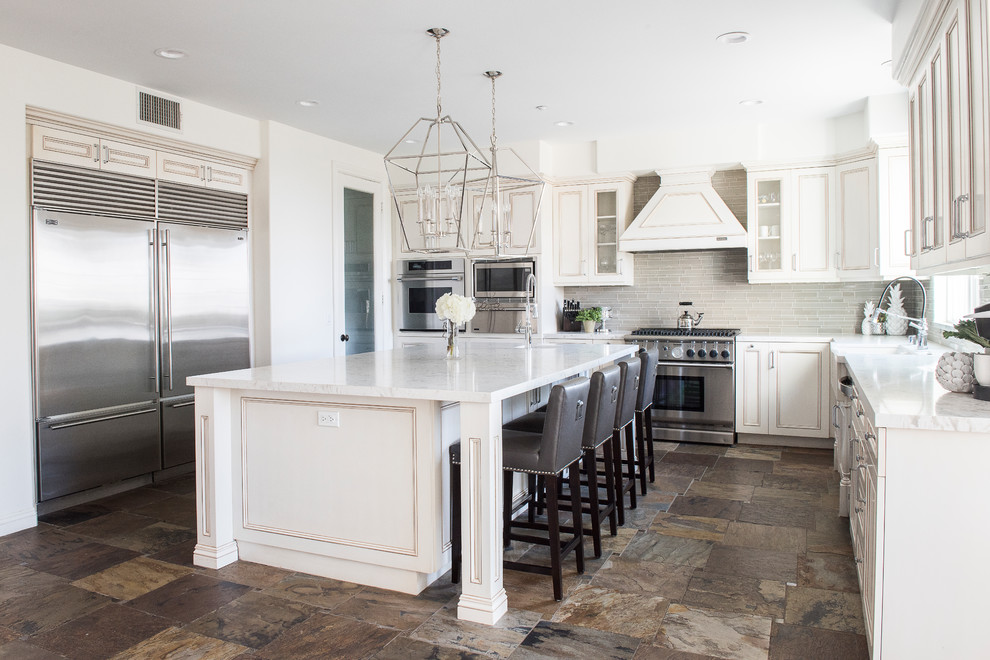Mid-sized transitional u-shaped separate kitchen in Orange County with a farmhouse sink, white cabinets, quartz benchtops, grey splashback, glass tile splashback, stainless steel appliances, slate floors, with island, brown floor, white benchtop and recessed-panel cabinets.