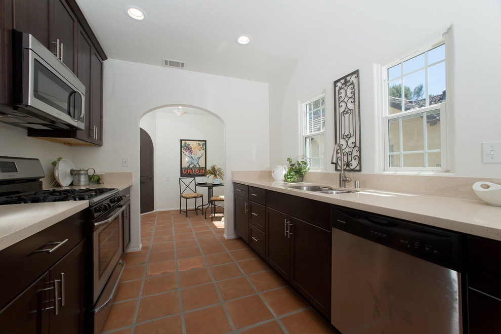 This is an example of a mid-sized galley eat-in kitchen in San Diego with an undermount sink, shaker cabinets, dark wood cabinets, quartz benchtops, beige splashback, stone slab splashback, stainless steel appliances, terra-cotta floors and no island.