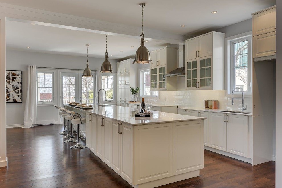 Large contemporary single-wall eat-in kitchen in Montreal with an undermount sink, raised-panel cabinets, white cabinets, quartz benchtops, white splashback, subway tile splashback, medium hardwood floors, with island and brown floor.