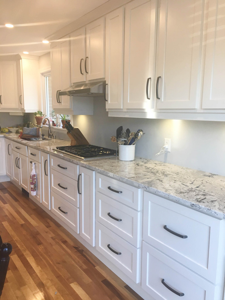 Inspiration for a mid-sized transitional u-shaped medium tone wood floor and brown floor eat-in kitchen remodel with recessed-panel cabinets, white cabinets, granite countertops, stainless steel appliances, an island and multicolored countertops