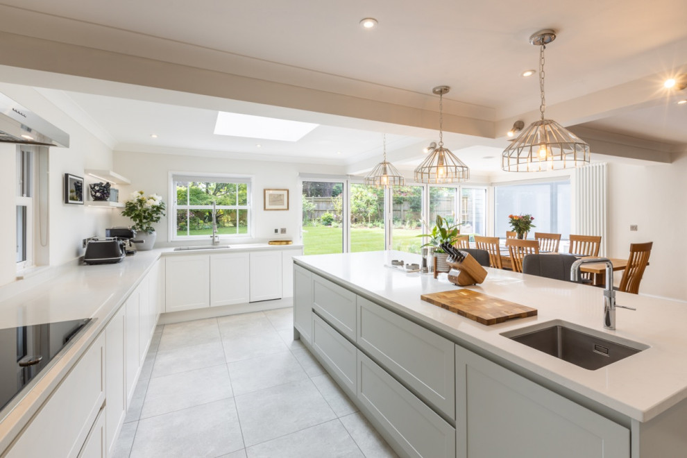This is an example of a large contemporary u-shaped open plan kitchen in Sussex with white cabinets, quartzite benchtops, with island and white benchtop.