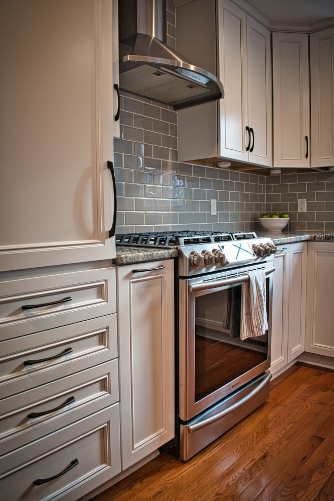 Mid-sized transitional l-shaped medium tone wood floor and brown floor eat-in kitchen photo with recessed-panel cabinets, white cabinets, granite countertops, gray backsplash, ceramic backsplash, stainless steel appliances, an island and multicolored countertops