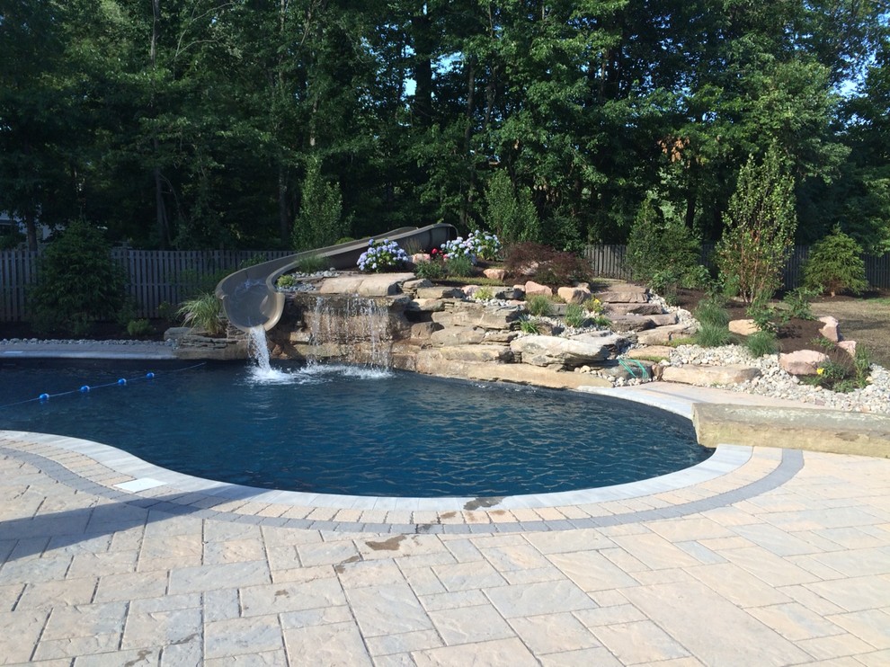 Photo of a large traditional backyard custom-shaped pool in New York with a water slide and concrete pavers.