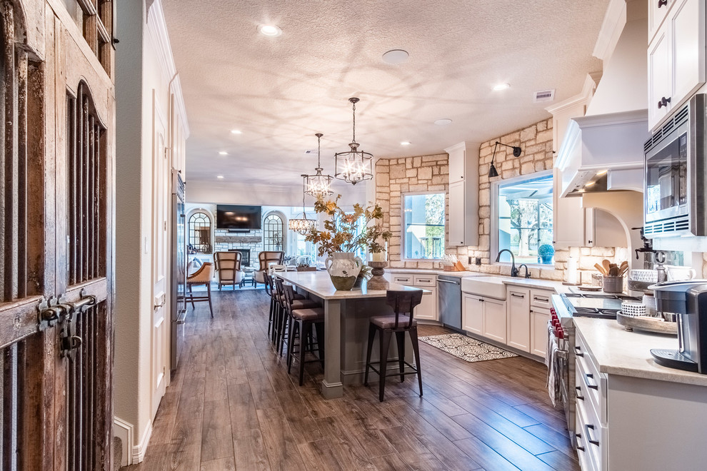 Photo of a large galley eat-in kitchen in Houston with a farmhouse sink, shaker cabinets, white cabinets, quartzite benchtops, multi-coloured splashback, stone tile splashback, stainless steel appliances, porcelain floors, with island, brown floor and multi-coloured benchtop.