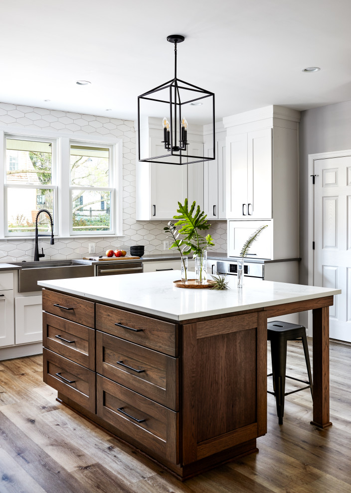 Inspiration for a large transitional u-shaped eat-in kitchen in DC Metro with a farmhouse sink, shaker cabinets, quartz benchtops, white splashback, ceramic splashback, stainless steel appliances, vinyl floors, with island, brown floor and white benchtop.