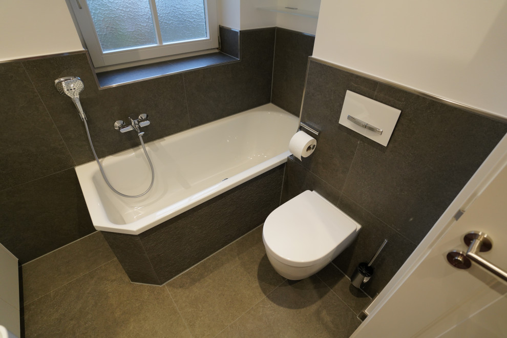 Badezimmer With flächenbündigen Schrankfronten, weißen Schränken, Eckbadewanne, Wandtoilette, schwarzen Fliesen, Steinfliesen, weißer Wandfarbe, Wandwaschbecken, schwarzem Boden, Einzelwaschbecken and schwebendem Waschtisch in Munich