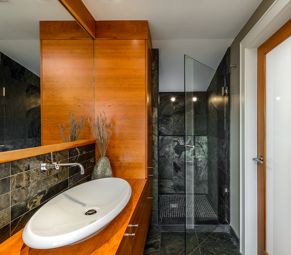 Photo of a contemporary bathroom in Vancouver with a vessel sink, flat-panel cabinets, medium wood cabinets, wood benchtops, an alcove shower and black tile.