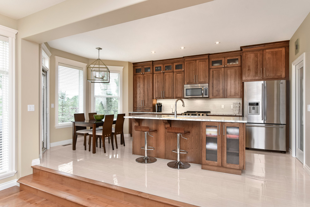 Open concept kitchen - large transitional single-wall porcelain tile open concept kitchen idea in Calgary with an undermount sink, medium tone wood cabinets, quartz countertops, beige backsplash, stainless steel appliances and an island