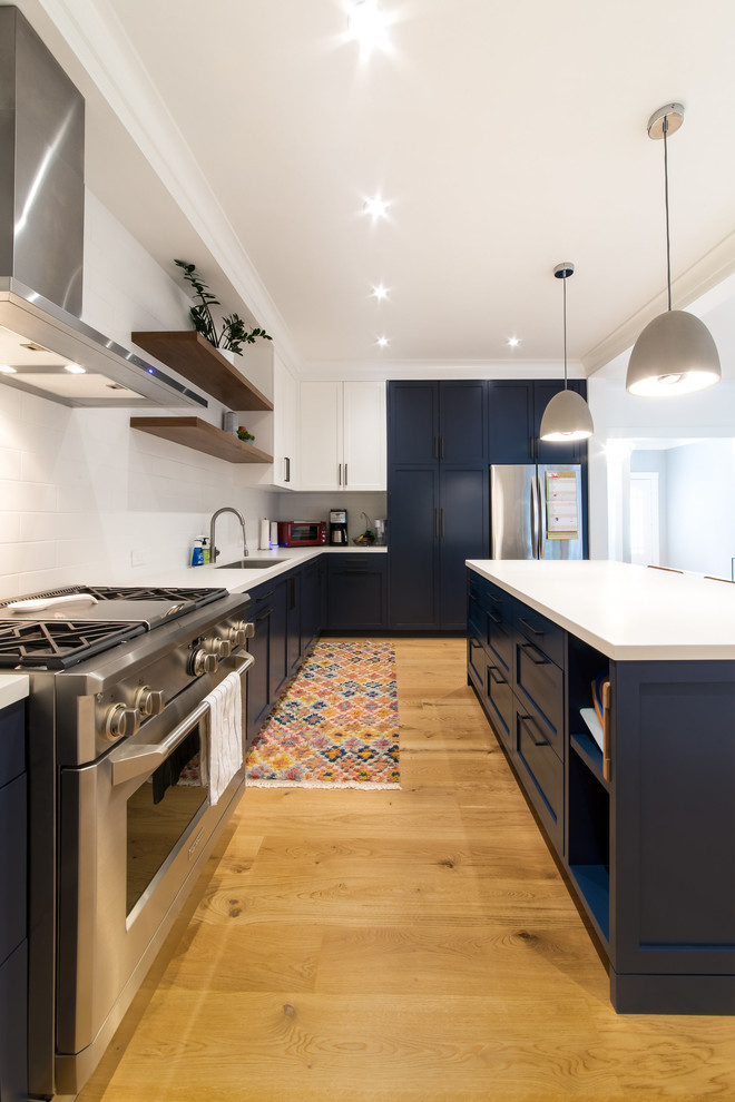 Design ideas for a mid-sized transitional l-shaped kitchen in San Francisco with an undermount sink, shaker cabinets, blue cabinets, white splashback, stainless steel appliances, medium hardwood floors, with island, brown floor, quartz benchtops and subway tile splashback.