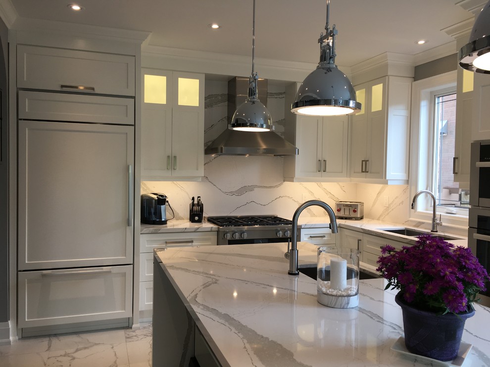 This is an example of a large transitional l-shaped separate kitchen in Toronto with an undermount sink, shaker cabinets, white cabinets, quartz benchtops, white splashback, stone slab splashback, stainless steel appliances, porcelain floors, with island, white floor and white benchtop.