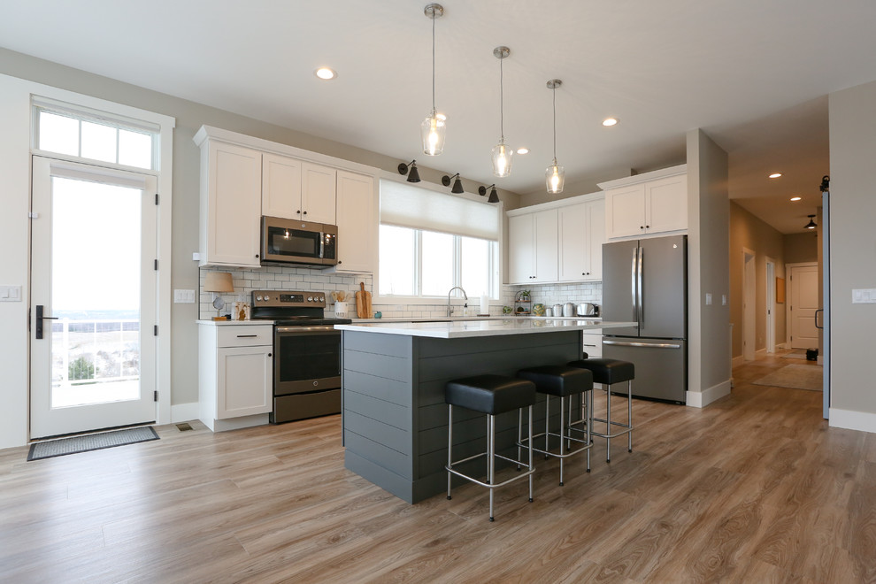 Example of a large transitional u-shaped light wood floor and brown floor eat-in kitchen design with an undermount sink, recessed-panel cabinets, white cabinets, quartz countertops, white backsplash, subway tile backsplash, stainless steel appliances, an island and white countertops